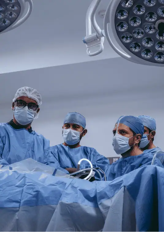 Equipo de cirujanos ortopedistas en quirófano bajo lámpara quirúrgica durante intervención de rodilla