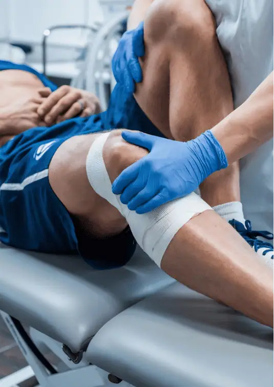 Especialista en traumatología examinando la rodilla vendada de un paciente en camilla médica